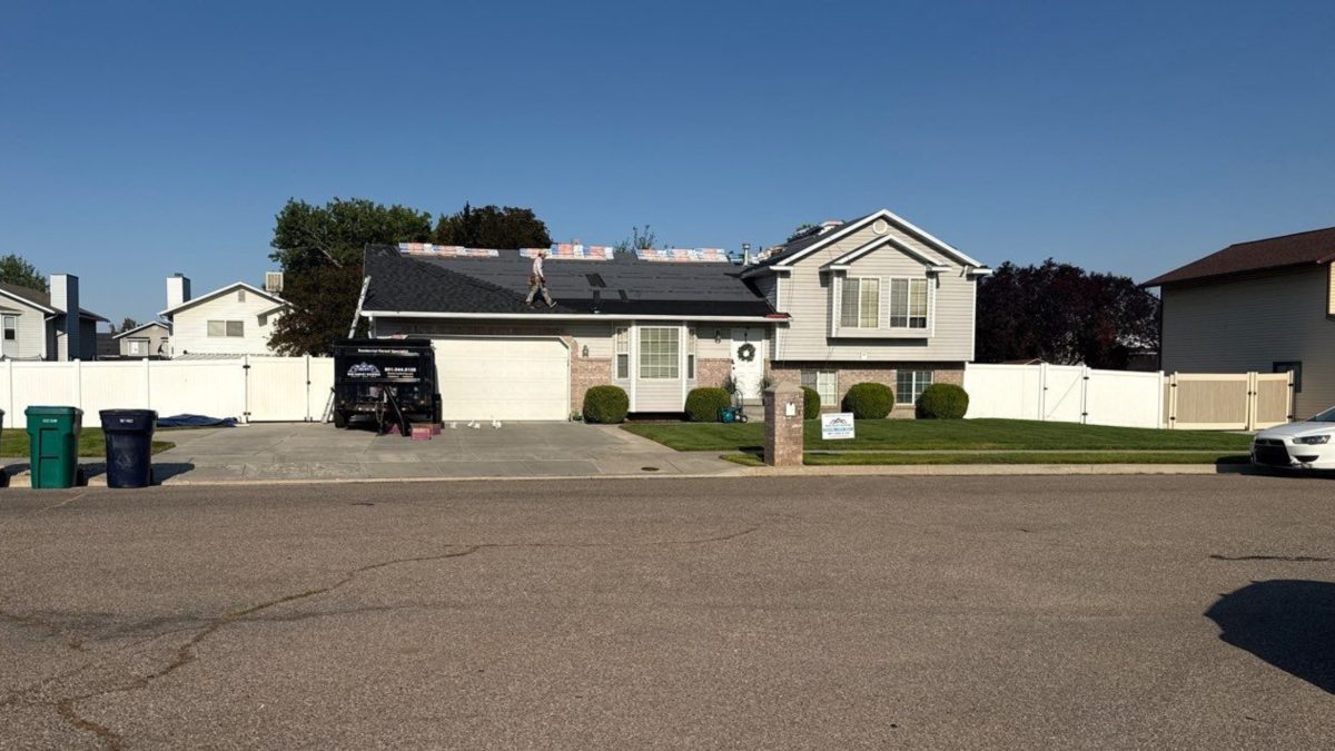 Roofing crew member walking a stripped roof deck with new shingle bundles staged along the ridge during a residential roof replacement in Northern Utah