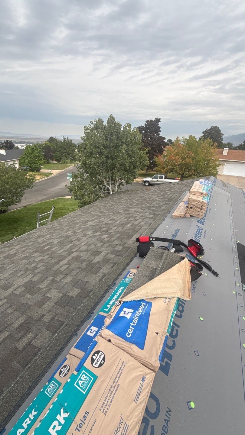 CertainTeed Landmark shingle bundles and CertainTeed underlayment staged along the ridge of a home during a roof replacement, with the valley visible in the background