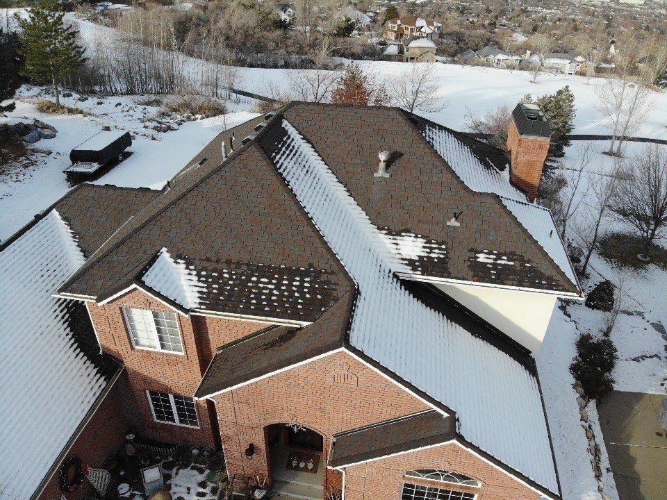 Aerial view of a snow covered home along the Wasatch Front where the shingle roof has melted clear while bands of snow remain along the colder eaves