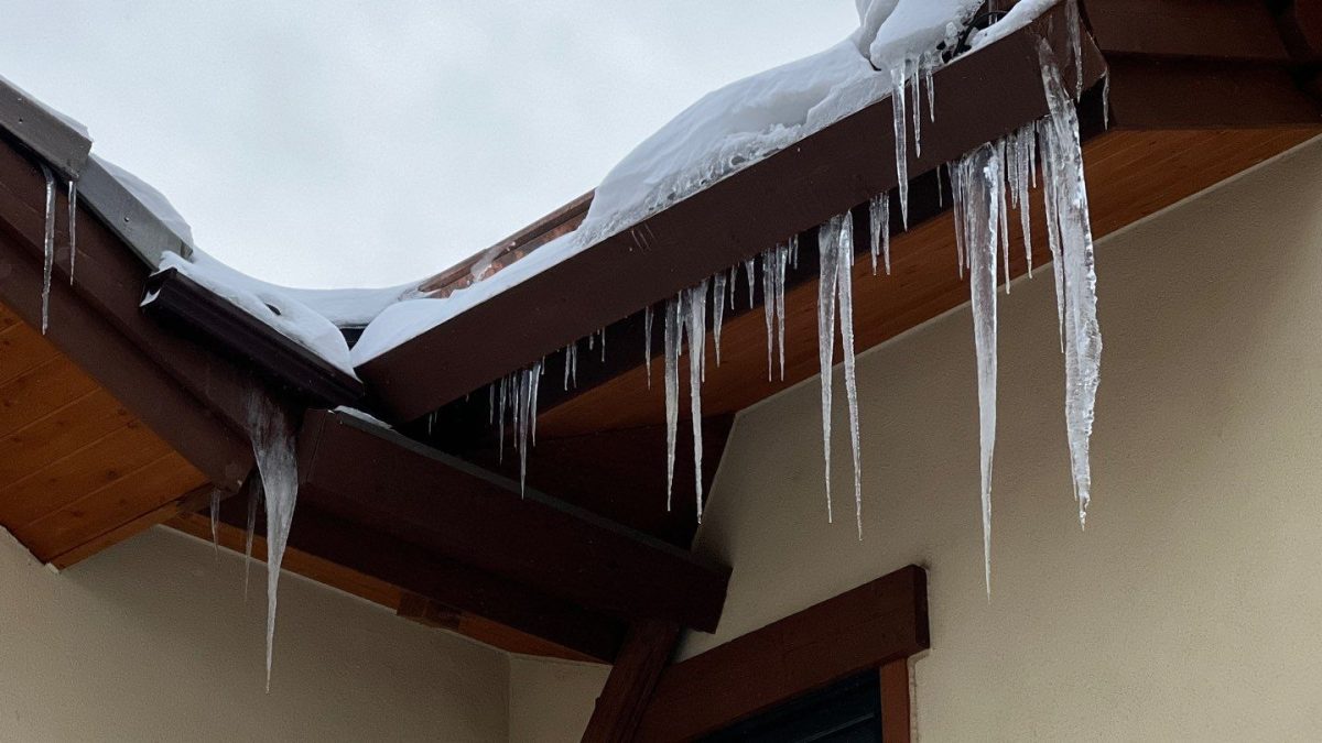 Thick icicles hanging from the eaves and gutter line of a Northern Utah home with snow still packed at the roof edge
